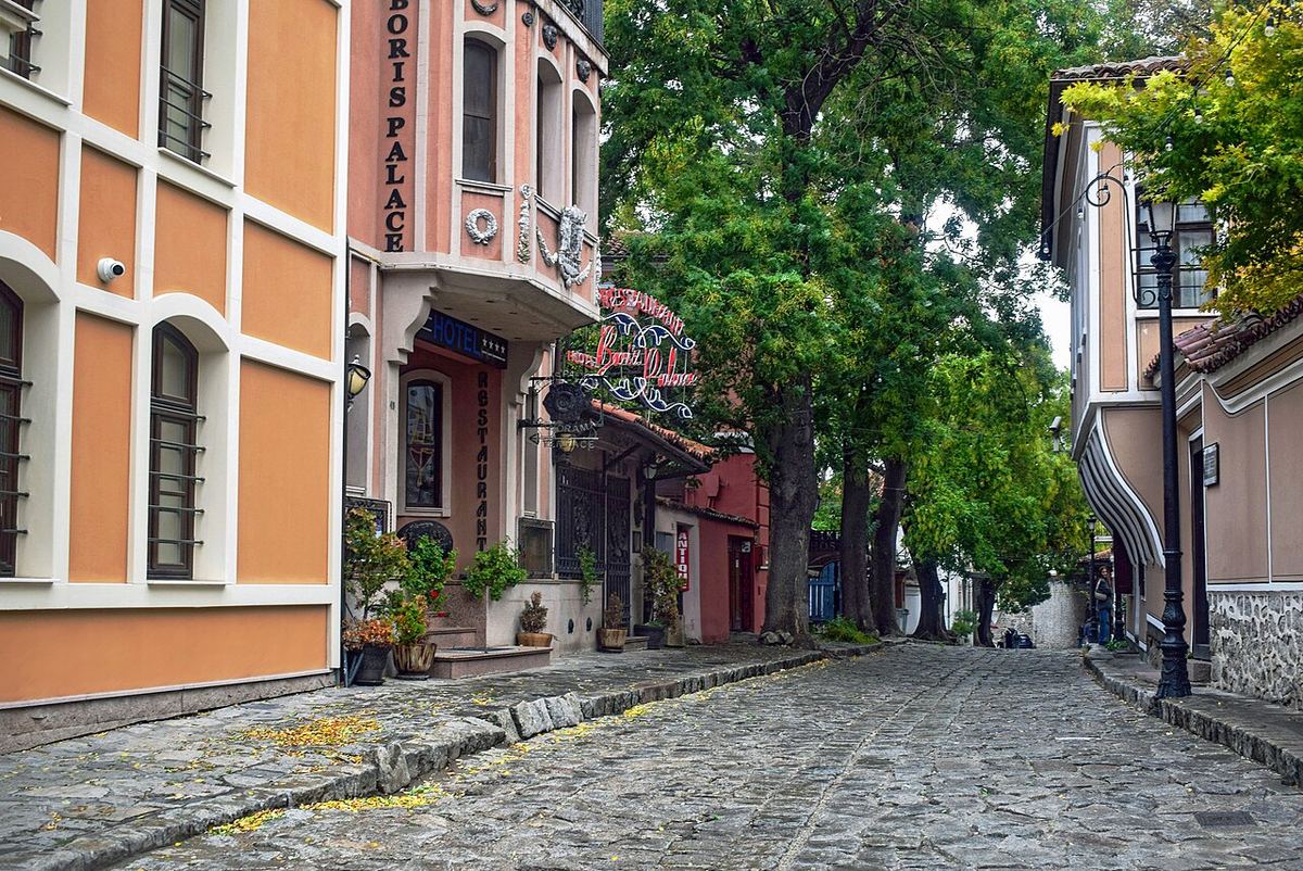 Широка калдъръмена улица в Стария Пловдив с цветни фасади и дървета